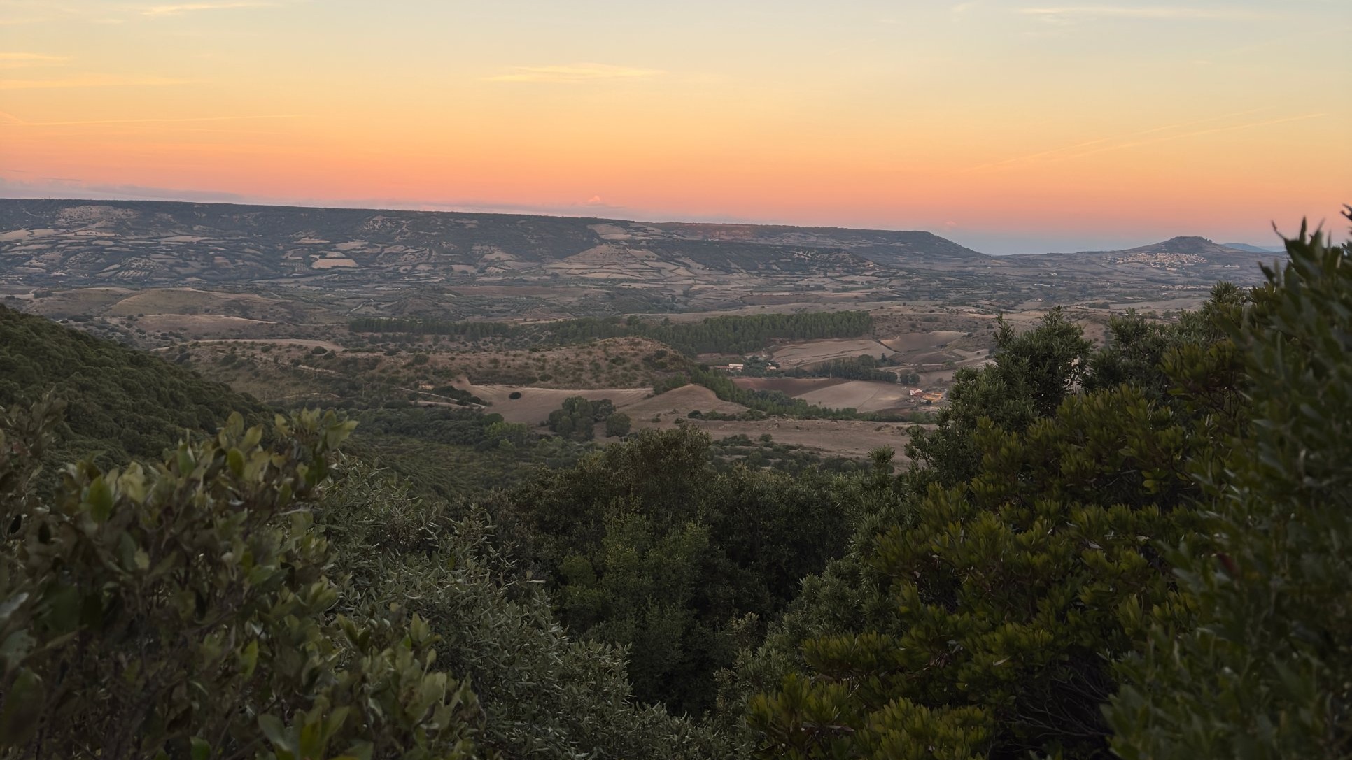 Panoramablick auf eine Naturlandschaft mit Hügeln, Vegetation und Sonnenuntergang. Sie können Wanderwege und einen dichten Wald sehen. Das Bild vermittelt ein Gefühl von Ruhe und Eintauchen in die wilde Natur.