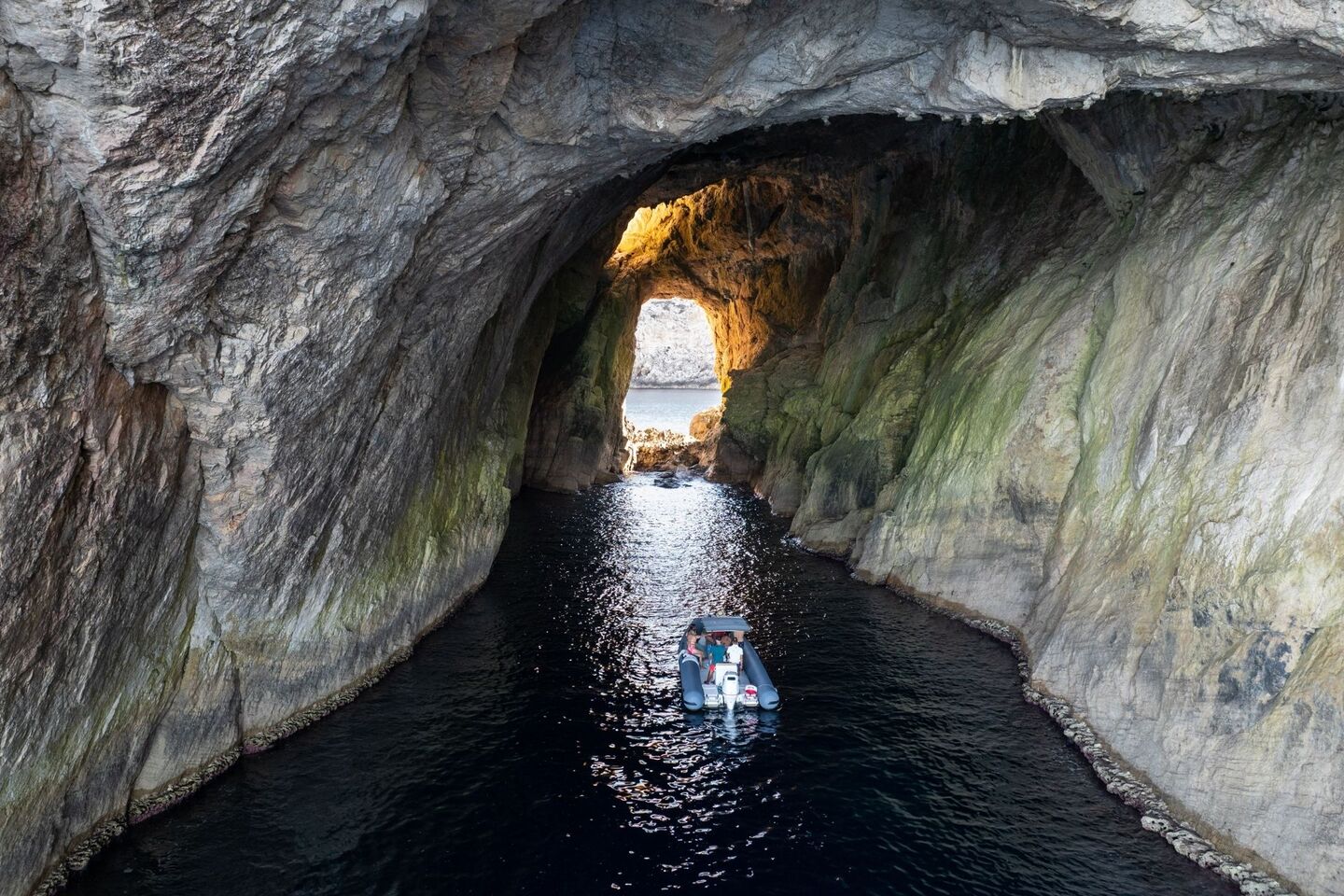 The dinghy goes into the cave of Faraglione di Foradada in Capo Caccia, Alghero